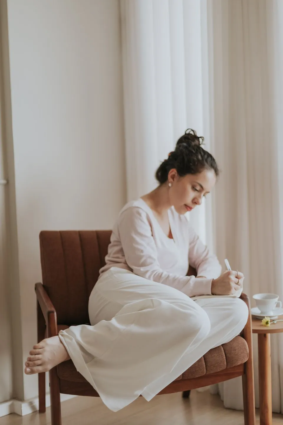 A woman writing in a journal in a peaceful, sunlit room.