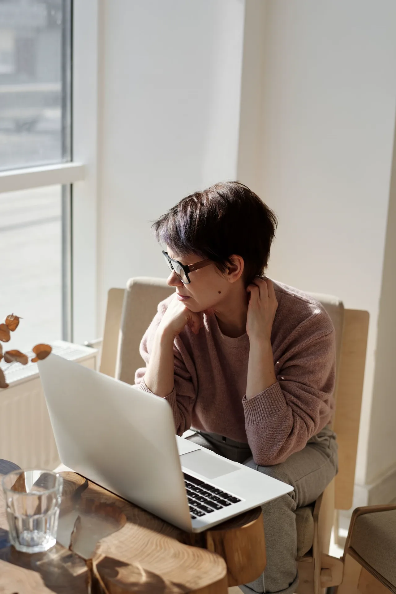 A woman pauses to think while working beside a sunny window